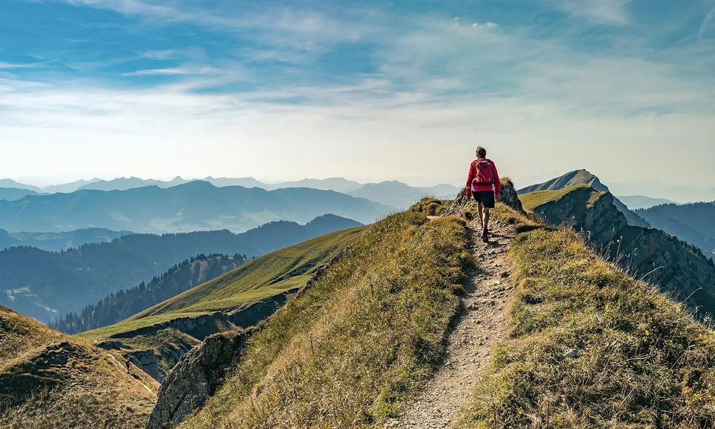 Person auf einem Berggipfel, mit einem Pfad, der in die Ferne zum Horizont führt