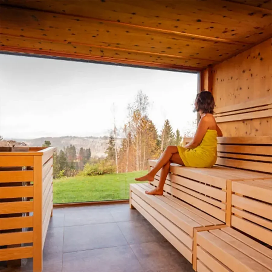 Frau in Handtuch sitzt in der Panoramasauna mit Blick in die Natur des Allgäus.